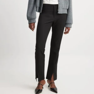 Svarta kostymbyxor med slits - Eleganta svarta kostymbyxor med hög midja och slits vid anklarna. Byxorna har en smickrande passform och är perfekta för en stilren look. Kombinera med klackar för en chic outfit.