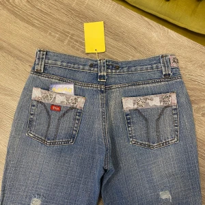 Park Flash Jeans 2000s Mcbling Rock Revival Bootcut Flare - Jeans med bootcut ifrån märket Park Flash. Har massa snygga detaljer runt bältet samt på fickorna. Dom är i nyskick och har kvar prislappen. Storlek 12 men kolla gärna måtten nedan!  I nytt skick  Storlek 12, kolla måtten  Mått Midja: 68cm runt om Innerbenslängd: 83cm Fotöppning: 27cm  Kolla gärna igenom mina andra annonser!