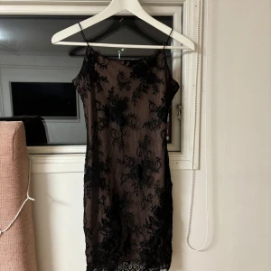 Svart spetsklänning från Divided - Elegant svart spetsklänning från Divided med ett nude-färgat foder. Klänningen har smala axelband och ett vackert blommigt spetsmönster. Perfekt för en stilfull kväll.