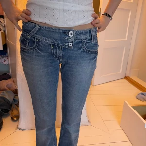 Blå jeans med unik knäppning - Snygga blå jeans från Laguna Moon med en cool, asymmetrisk knäppning framtill. De har en straight passform och klassiska femficksdetaljer. Perfekta för en avslappnad stil med en twist. Alla tre knappar finns de var bara inte möjligt att knäppa knappen i mitten vid tillfället då jeansen är för små för oss!