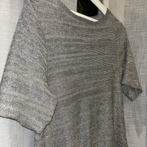 Glittrig grå topp - Snygg glittrig grå topp med korta ärmar. Perfekt för en kväll ute eller en festlig tillställning. Toppen har en lös passform och är tillverkad i ett glittrande material som fångar ljuset fint.