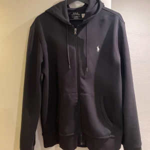 Svart hoodie från Polo Ralph Lauren - Säljer min svarta zip hoodie från Polo Ralph Lauren i nyskick som inte kommer till användning. Tröjan är nästan aldrig använd och är perfekt för en avslappnad stil. Nypris 1700. Mitt pris 950