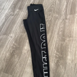 Svarta leggings från Nike - Säljer ett par svarta leggings från Nike i bra skick. De har en vit logga på ena benet och är perfekta för träning. Materialet är stretchigt och bekvämt, vilket gör dem idealiska för både gymmet och löprundan. Passformen är tight och de sitter snyggt på kroppen.