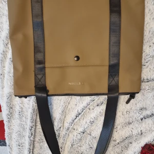 Beige Axelremsväska från Tretorn - Säljer en snygg beige Axelremsväska Tretorn i syntetmaterial. Den har svarta axelremmar och en praktisk dragkedja upptill. Perfekt för vardagsbruk eller utflykter. Axelremsväska i nytt skick och har en stilren design med en knappdetalj på framsidan. 