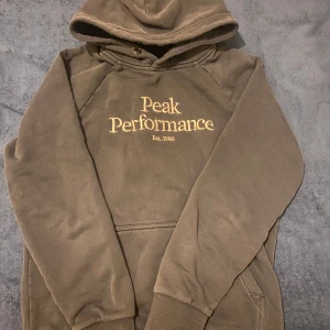 Svart och litet mörkblå hoodie från Peak Performance - Säljer en brun hoodie från Peak Performance i mycket bra skick. Den har en klassisk design med logga på bröstet och en mysig luva. Perfekt för höst och vinter, och passar både till vardags och träning. Storleken (S). I bilden ser färgen konstigt ut men den är inte så verkligen.