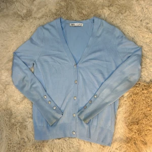 Ljusblå kofta från Zara - Säljer en superfin ljusblå kofta från Zara. Den har en v-ringad design med snygga knappar framtill och långa ärmar. Dock finns det små vita prickar på baksidan av fotar men det tänker man inte på så mycket spelciellt om man har håret nere 🩵