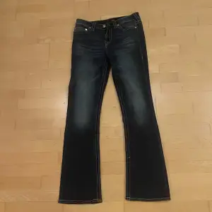 Säljer ett par snygga True Religion Becca jeans i bootcut-stil. De är mörkblå med klassisk femficksdesign och har en medelhög midja. Perfekta för en avslappnad men stilren look. Passar både till vardags och fest!