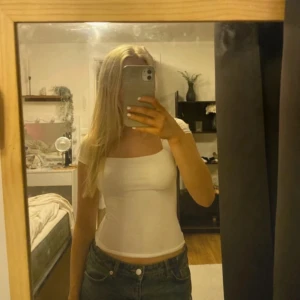 Vit ärmlös tubtopp - Säljer en snygg vit kortärmad i tight passform. Perfekt för sommaren eller en utekväll. Toppen är enkel och stilren, vilket gör den lätt att matcha med olika outfits. Den är i mycket bra skick och redo för nya äventyr! Tunnt material