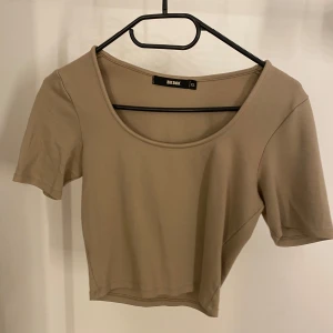 Beige kortärmad topp från Bik Bok - Säljer en stilren beige topp från Bik Bok i storlek XS. Den har en enkel design med korta ärmar och en rund halsringning. Perfekt för både vardag och fest! 🥳