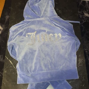 Blå velourset från Juicy Couture - Säljer ett supermysigt blått velourset från Juicy Couture. Hoodien har en dragkedja och glittrande Juicy-text på ryggen. Byxorna är matchande med samma bling på baksidan. Perfekt för chill dagar eller när du vill känna dig extra glam. 🦋