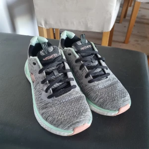 Grå sneakers från Skechers - Säljer ett par grå Skechers sneakers i mycket bra skick. De har en snygg stickad look med svarta snören och mintgröna detaljer. Sulan är vit med rosa inslag och märkt 'Ultra Light' för extra komfort. Perfekta för träning eller vardagsbruk!