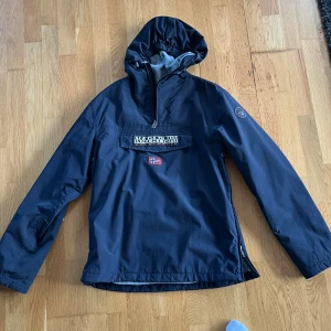 Svart jacka från Napapijri - Säljer en svart Napapijri jacka i mycket bra skick. Den har en praktisk huva och en stor ficka framtill med dragkedja. Insidan är fodrad med mjuk fleece för extra värme. Perfekt för höst och vår! 🖤