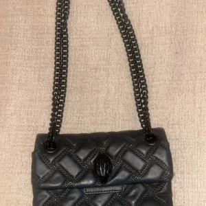 Svart quiltad axelväska från Kurt Geiger - Snygg svart axelväska från Kurt Geiger i skinn. Väskan har en kedjerem och stängs med tryckknappar. Säljer då jag har köpt en annan väska som jag använder mer ! 💕💕 skriv för frågor eller fler specifika bilder. Köptes för 2000 kr 