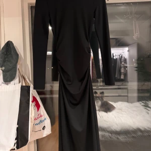 Svart långklänning med rynkdetaljer - Elegant svart långklänning med långa ärmar och snygga rynkdetaljer på sidan. Perfekt för en festlig kväll eller en formell tillställning. Klänningen har en figurnära passform som framhäver silhuetten. Klänningen är en xxs, men passar xs-s iåmed stretchen!