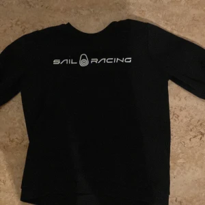 Svart tröja från Sail Racing - Säljer en svart tröja från Sail Racing i bra skick. Den har en stilren design med Sail Racing-loggan tryckt på framsidan. Perfekt för både vardag och fritid. Passar bra till jeans eller chinos för en avslappnad look. Kan diskutera pris!!