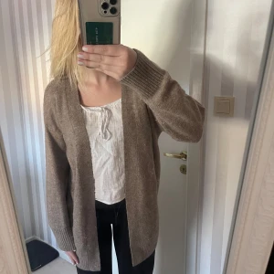 Beige stickad kofta - Säljer en supermysig beige stickad kofta. Perfekt för kyliga höst- och vinterdagar. Den har en avslappnad passform och långa ärmar med ribbade muddar. Perfekt att slänga över en t-shirt eller blus för extra värme. 