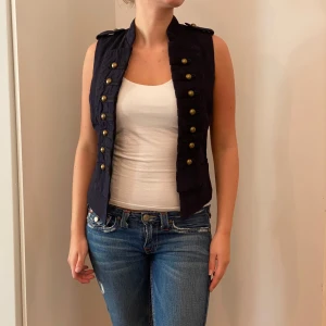 Svart väst från La Redoute - Snygg svart väst från La Redoute med dubbla rader av knappar framtill. Perfekt för att ge en stilren touch till din outfit. Västen är i normal passform och passar bra till både vardag och fest. Ett måste i garderoben för den modeintresserade!