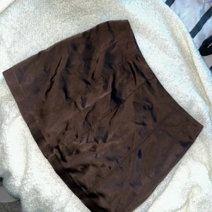 Brun satinkjol  - Snygg brun satinkjol i kort modell. Perfekt för höst och vinter med ett par snygga stövlar. Kjolen har en stilren design utan mönster eller detaljer, vilket gör den lätt att matcha med olika toppar. Ett måste i garderoben för en chic look! Aldrig använd.