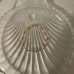 Färgglatt pärlarmband med bokstäver - Säljer ett supergulligt armband med färgglada pärlor i lila och gult. Armbandet har bokstavspärlor som bildar 'FBK'. Perfekt för att ge en personlig touch till din stil! 🟣🟡
