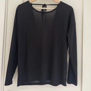 Svart långärmad topp från Jacqueline de Yong - Säljer en stilren svart långärmad topp från Jacqueline de Yong i storlek XS. Toppen har en öppen rygg med knytband och är gjord i ett lätt och luftigt material. 
