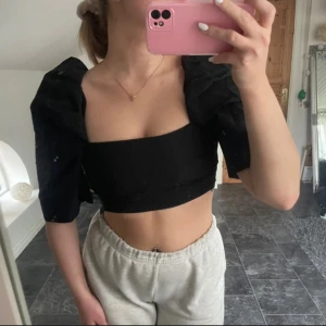 Svart croppad topp - Säljer en svart croppad topp med puffiga ärmar. Toppen är tight och har en stilren design som passar perfekt för festliga tillfällen. Den ger en elegant look.