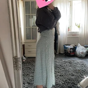 Blommig långkjol med slits - Säljer en superfin långkjol med ett sött blommigt mönster i ljusgrönt och vitt. Kjolen har en elegant slits på sidan som ger en extra touch. Perfekt för vår och sommar, och funkar både till vardags och fest. Kjolen är i bra skick och har en normal passform.