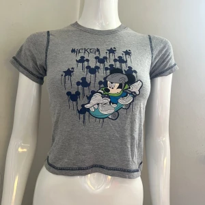 Grå babytee med Disney-tryck - unik grå Musse-babytee med mörkblå kontrast stitches. Sitter snyggt på Xs-S.