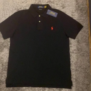 Ralph Lauren Piké - Fet Ralph Lauren piké, svart med röd loga. Skick 8/10. Storlek M. Perfekt för alla tillfällen, ett stilrent plagg som passar alla. - PRIS går att diskutera.