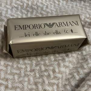 Säljer en elegant parfym från Emporio Armani. Förpackningen är i en lyxig guldton med märkets logga och texten 'lei/elle/she/ella/女'. Perfekt för den som vill ha en sofistikerad doftupplevelse. Förpackningen är stilren och modern, vilket gör den till en perfekt present eller tillägg till din egen samling.