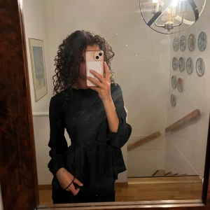 Svart blouse med dekoration - En svart blus med en kjol-aktig nederdel och blom-aktiva dekorationer i mitten av blusen. 