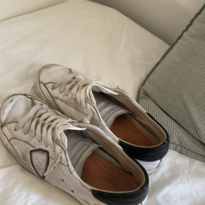 Vita sneakers med svarta detaljer - Säljer ett par vita sneakers med svarta detaljer. De har snörning och är i välanvänt skick. Perfekta för en casual look! sulan e lite sönder men går jätte bra att gå i