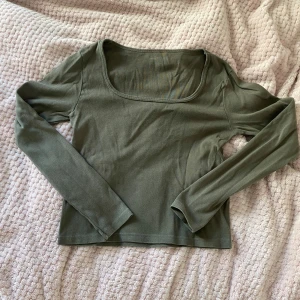 Olivgrön långärmad topp - Säljer en olivgrön långärmad topp i mjukt material. Toppen har en enkel och stilren design med rund halsringning. Perfekt för vardagsbruk eller att matcha med ett par jeans för en avslappnad look.
