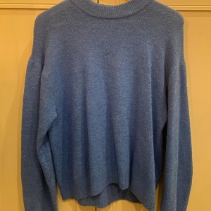 Blå stickad tröja från H&M - Säljer en supermysig blå stickad tröja från H&M. Perfekt för kyliga dagar med sin mjuka och bekväma passform. Tröjan har långa ärmar och en ribbad krage som ger en stilren look. Passar perfekt till både jeans och kjol!