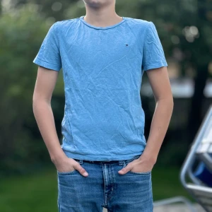 Blå t-shirt från Tommy Hilfiger - Säljer en snygg blå t-shirt från Tommy Hilfiger i storlek 152. Den är gjord av ekologisk bomull och har en liten broderad logga på bröstet. Perfekt för en avslappnad stil! Skick 8/10