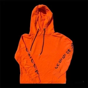 Orange hoodie med tryck på ärmarna - Säljer en cool orange hoodie med svart tryck längs ärmarna. Den har en klassisk huva med dragsko och är perfekt för en avslappnad stil. Passar bra till både vardag och chillhäng. Skön och bekväm att ha på sig!