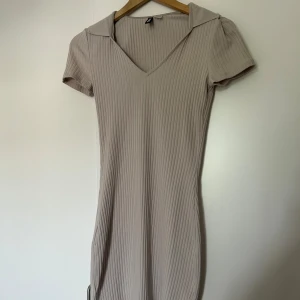 Beige ribbad klänning från Divided - Säljer en superfin beige ribbad klänning från Divided. Den har en v-ringad hals och korta ärmar, perfekt för både vardag och fest. Klänningen är i storlek S och har en tight passform som framhäver figuren. Materialet är mjukt och stretchigt, vilket gör den bekväm att bära hela dagen. Passar XS-M