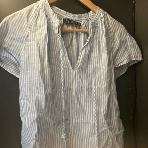 Blå- och vitrandig blus från Polo Ralph Lauren - Säljer en superfin blå- och vitrandig blus från Polo Ralph Lauren. Den har korta ärmar och en avslappnad passform med en liten v-ringning. Perfekt för vår och sommar!