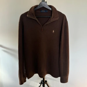 Brun tröja från Polo Ralph Lauren - Säljer en snygg brun tröja från Polo Ralph Lauren. Den har en dragkedja vid halsen och är perfekt för höst och vinter. Tröjan är långärmad och har en normal passform. Den är i bra skick och passar både till vardags och lite finare tillfällen.