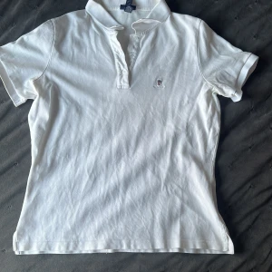 Vit kortärmad pikétröja från GANT - Säljer en klassisk vit pikétröja från GANT i storlek L. Tröjan är kortärmad och har en broderad logga på bröstet. Perfekt för en stilren och avslappnad look. Bra skick men har små fläckar på backsidan som du kan se på i sista bilden