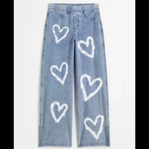Blå jeans med hjärtmönster - Säljer ett par supercoola blå jeans med stora vita hjärtan tryckta över hela byxorna. De har en avslappnad passform och raka ben, vilket gör dem både bekväma och trendiga. Perfekta för att ge din outfit en unik touch! 💙
