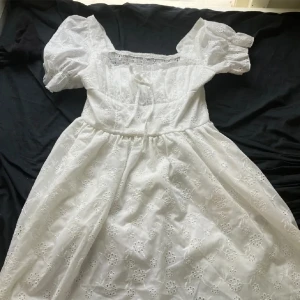 Vit klänning med puffärmar - Säljer en superfin vit klänning med puffärmar och ett vackert broderat blommönster. Klänningen har en smockad överdel som ger en tight passform upptill och en lösare kjol som faller fint. Perfekt för sommarens alla fester och midsommarfirande! 🌸