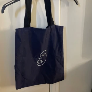 Tygpåse - En marinblå tygpåse med broderi på med ett svart band
