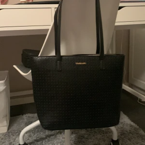 Svart axelväska från Vezzano - Säljer en snygg svart axelväska från Vezzano. Väskan är i fejkskinn med ett coolt mönster och har en dragkedja på baksidan. Perfekt för skolan då den får plats med dator! 🖤