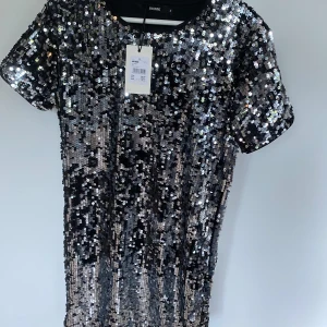 Glittrig klänning från Bik Bok - Säljer en superglittrig klänning från Bik Bok i storlek S. Den är täckt med massor av paljetter som verkligen fångar ljuset. Perfekt för en fest eller nyårsafton! Klänningen har korta ärmar och en bekväm passform. ALDRIG använd