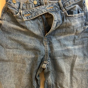 Blå jeans med råa kanter - Säljer ett par klassiska blå jeans med en cool, avslappnad stil. De har en rak passform och är tillverkade i slitstarkt denim. Jeansen har är lite söndriga vid fötterna då dom är långa. Jag är 174cm och dom hänger på mina fötter.