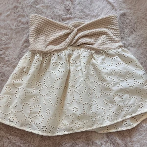 Vit kjol med virkad midja - Säljer en superfin beige topp med en bred virkad topp i beige. toppen har ett vackert blommigt broderi och är perfekt för sommaren. Den är i nyskick och passar perfekt till både vardag och fest. Storleken är dam xs.