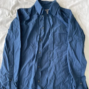 Blå randig skjorta från H&M - Säljer en blå randig skjorta från H&M i storlek M. Skjortan har långa ärmar och knappar hela vägen ner. Perfekt för både vardag och fest. Den är i bra skick och väldigt bekväm att ha på sig. Passar bra till jeans eller kostymbyxor. Frågor? Skriv!