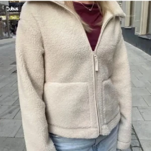 Beige teddyjacka med dragkedja - Mysig beige teddyjacka med dragkedja framtill och två stora fickor. Perfekt för kyliga dagar med sin mjuka och varma känsla. Jackan har en hög krage och långa ärmar.säljer den pga den är för små för mig, Det finns i strl xs och är nyskick.obs bilden är lånade 
