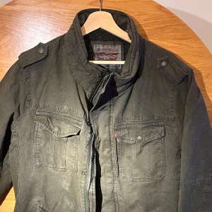 Grön jacka från Levi Strauss & Co. - Säljer en grön jacka från Levi Strauss & Co. med dragkedja och knappar. Jackan har långa ärmar och två bröstfickor med lock. Perfekt för höst och vår.