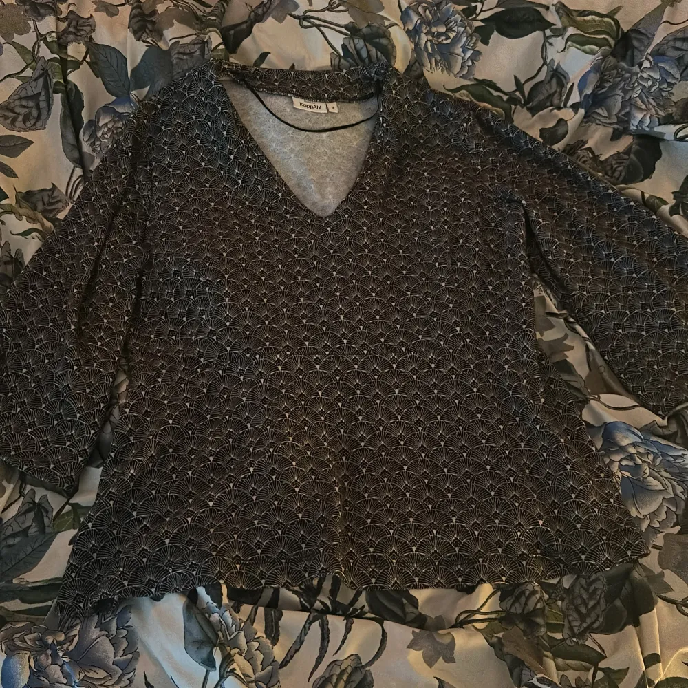 Säljer en svart topp från KappAhl med ett elegant mönster i vitt. Toppen har trekvartsärmar och en v-ringad hals. . Puserot.
